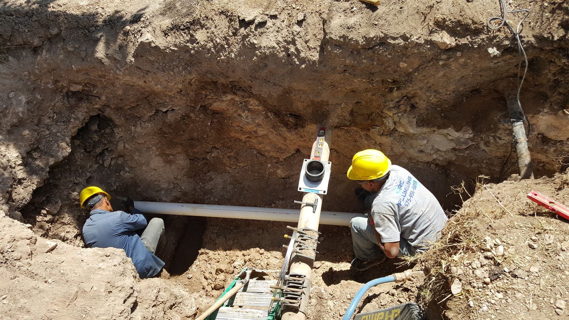 Two men are working on a pipe in the dirt.