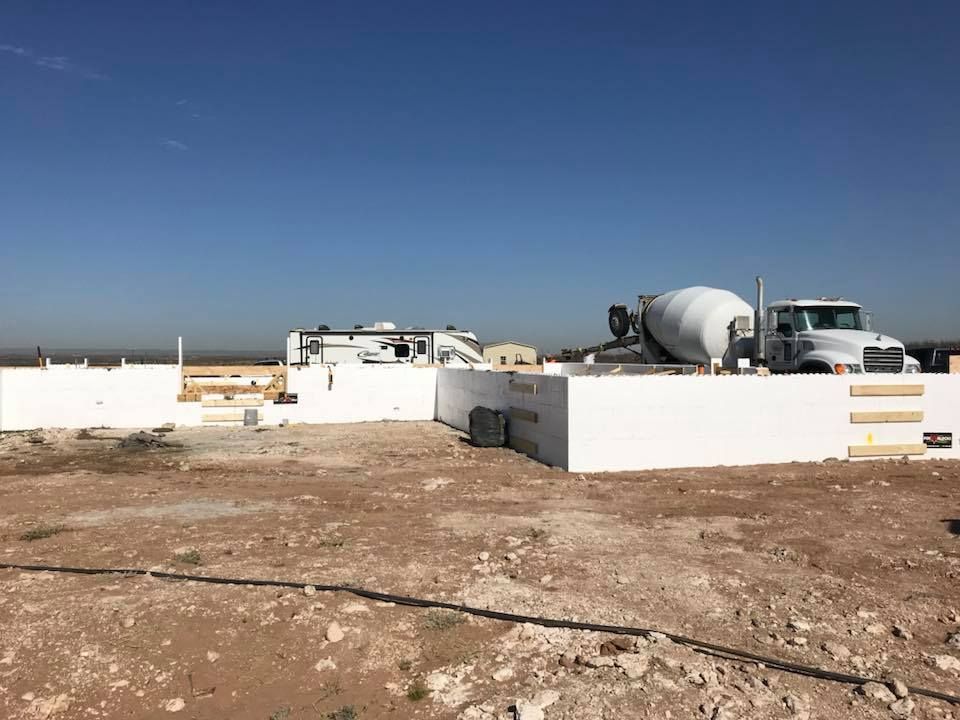 A concrete mixer truck is sitting in the middle of a dirt field.