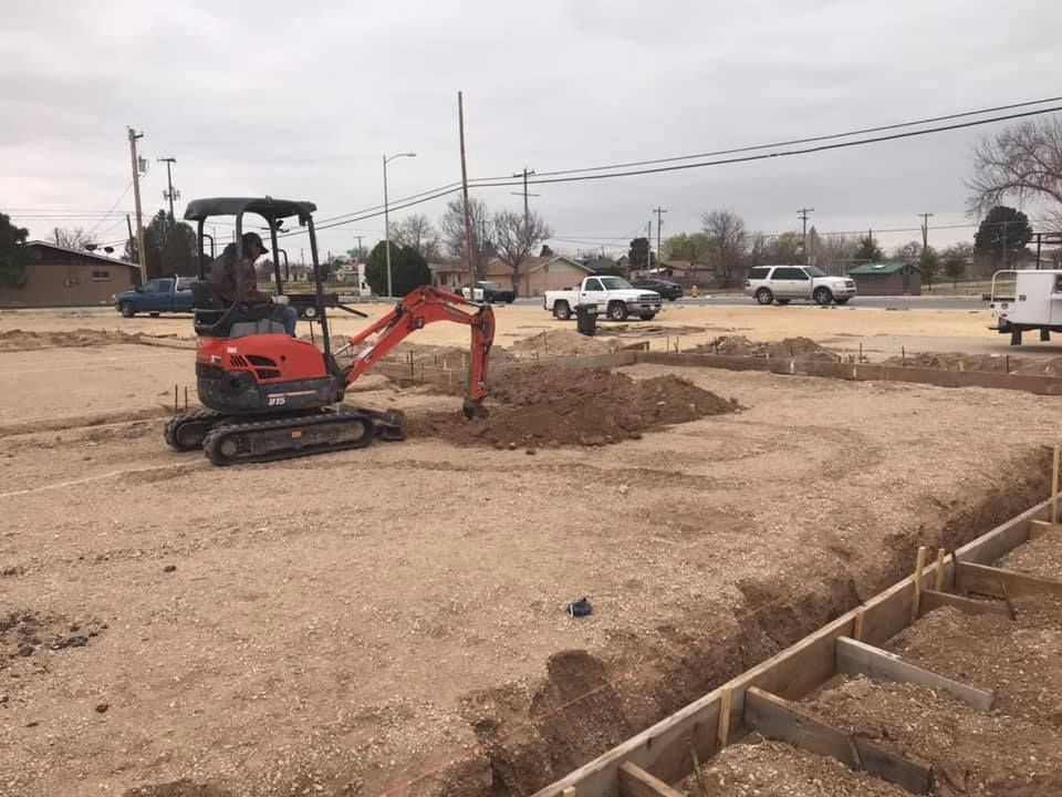 A man is driving an excavator in a dirt field.