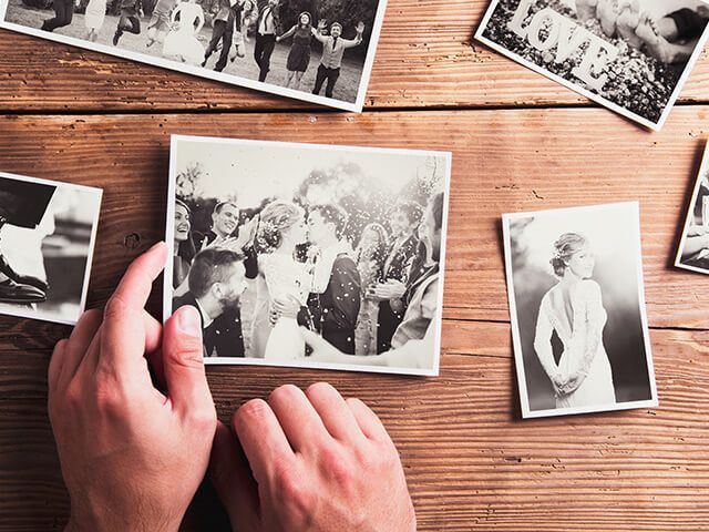 A person is holding a picture of a bride and groom on a wooden table.