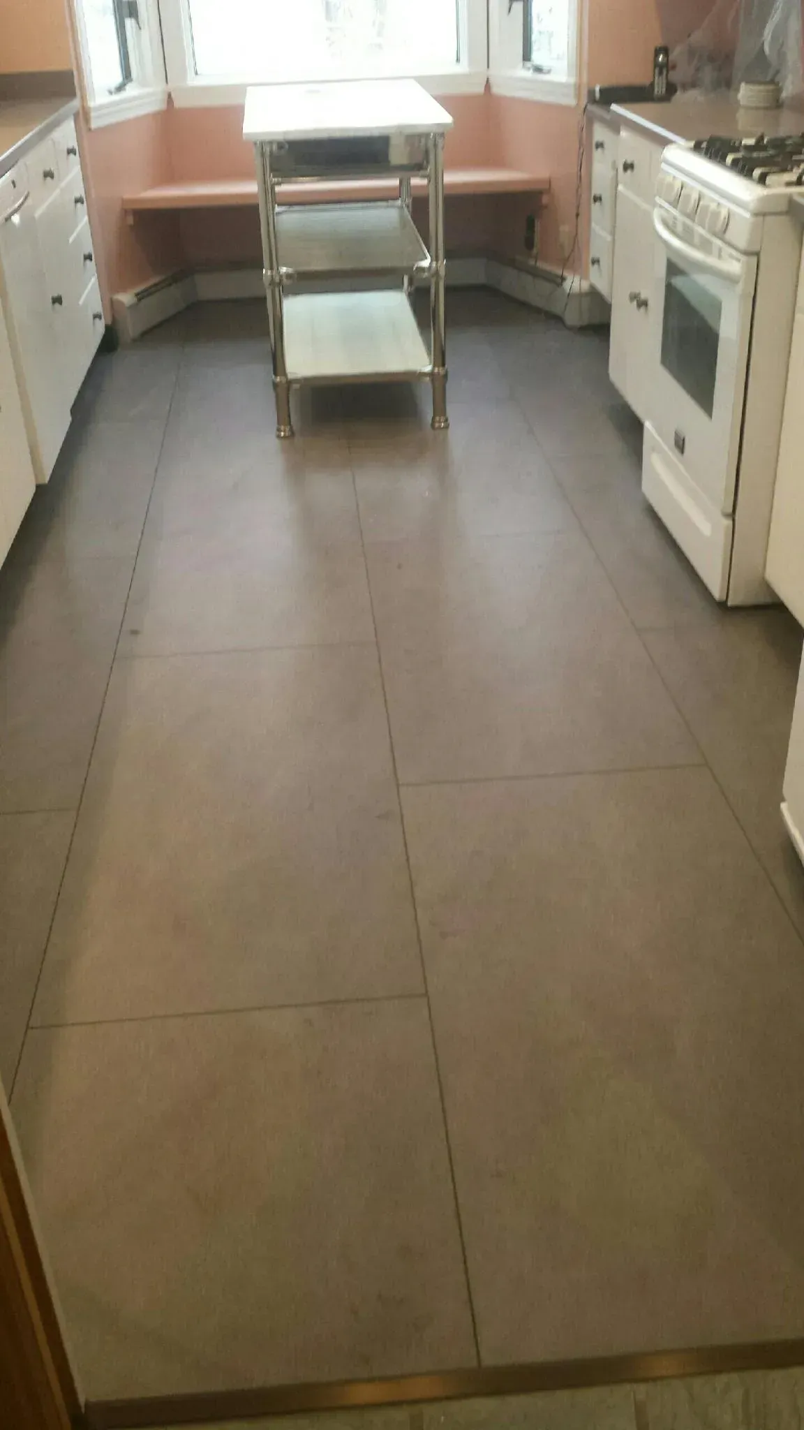 A kitchen with a tiled floor , white cabinets , a stove and a table.