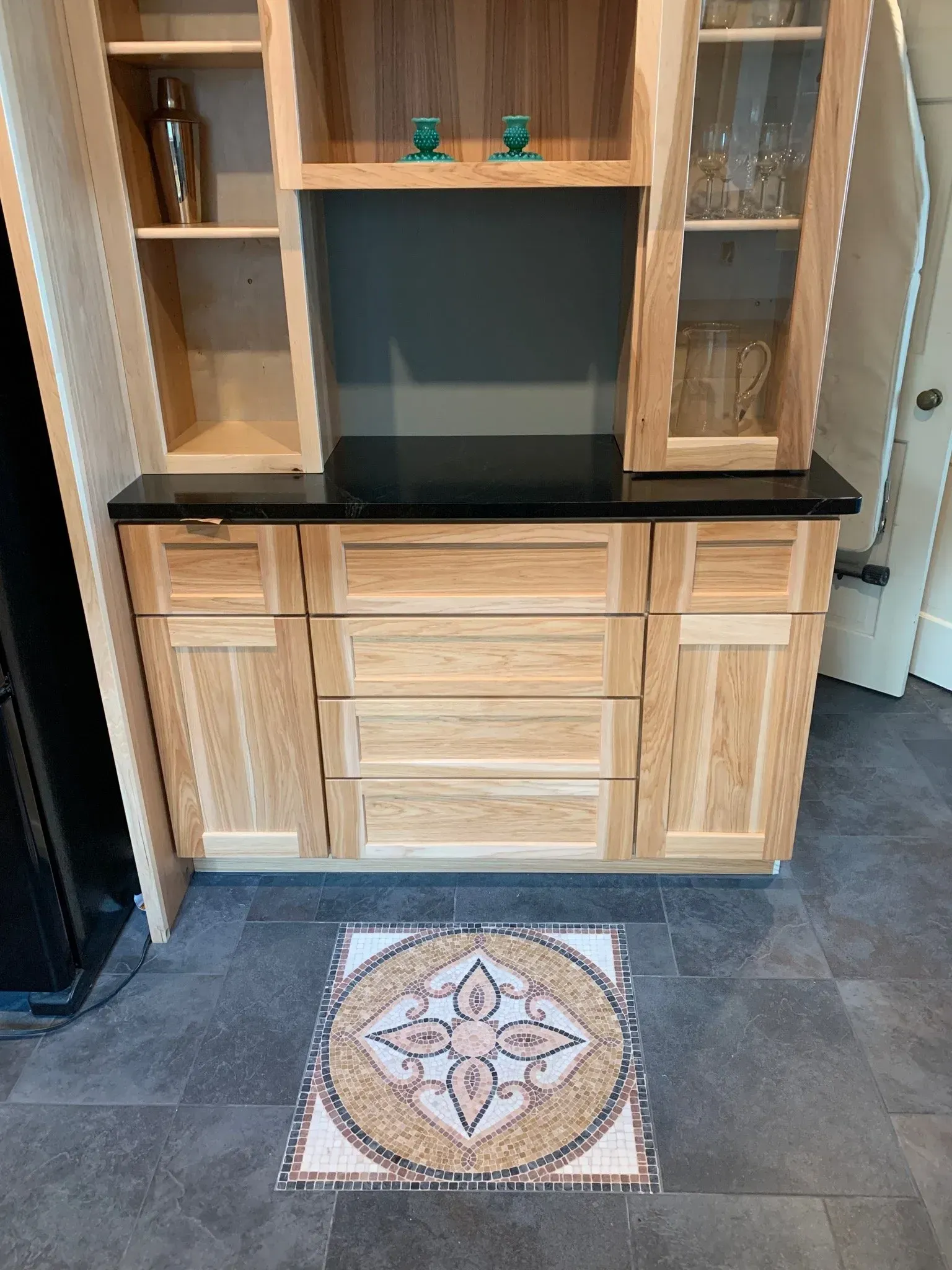 A wooden cabinet with a black counter top and a mosaic tile floor.