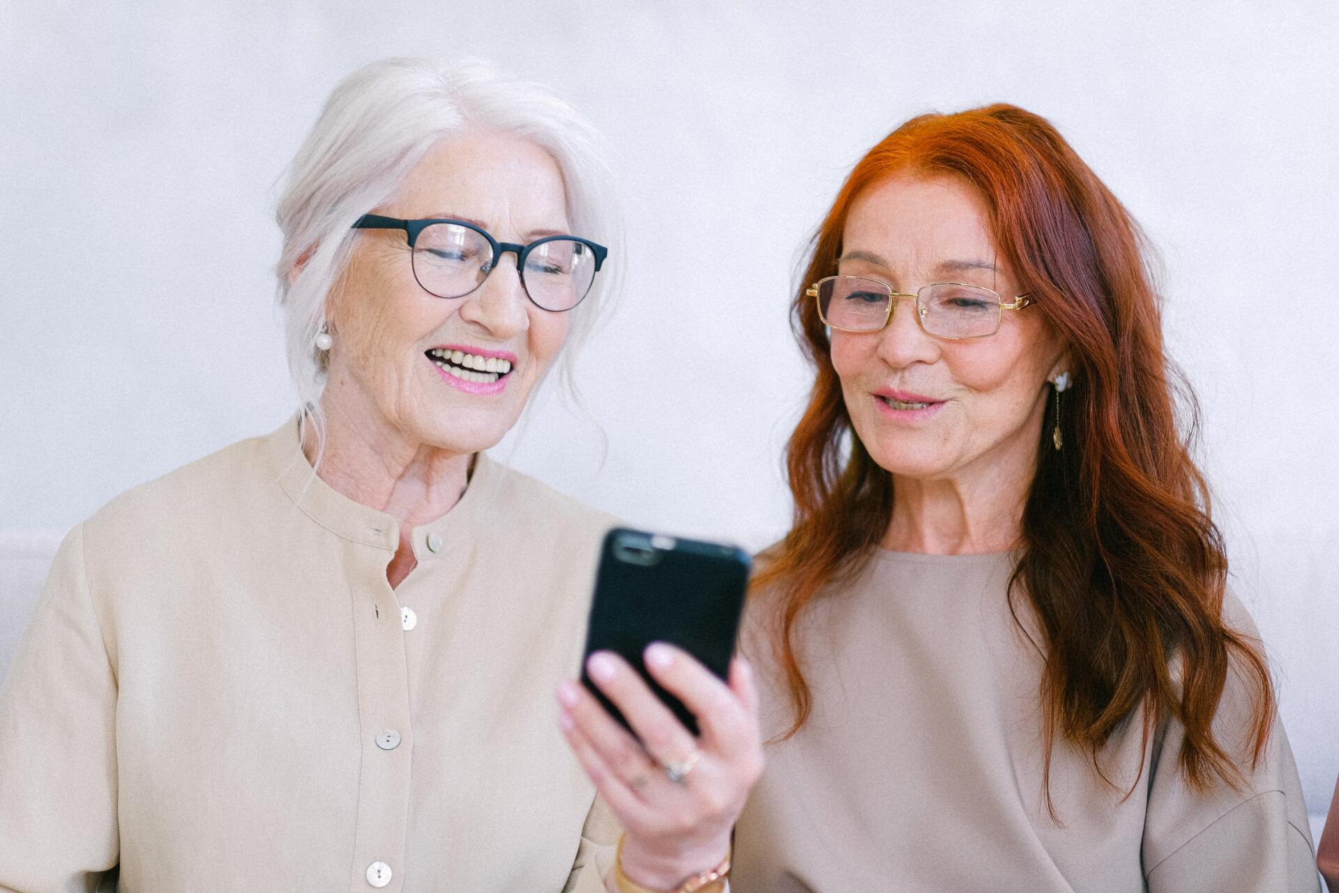 Two older women are looking at a cell phone together.