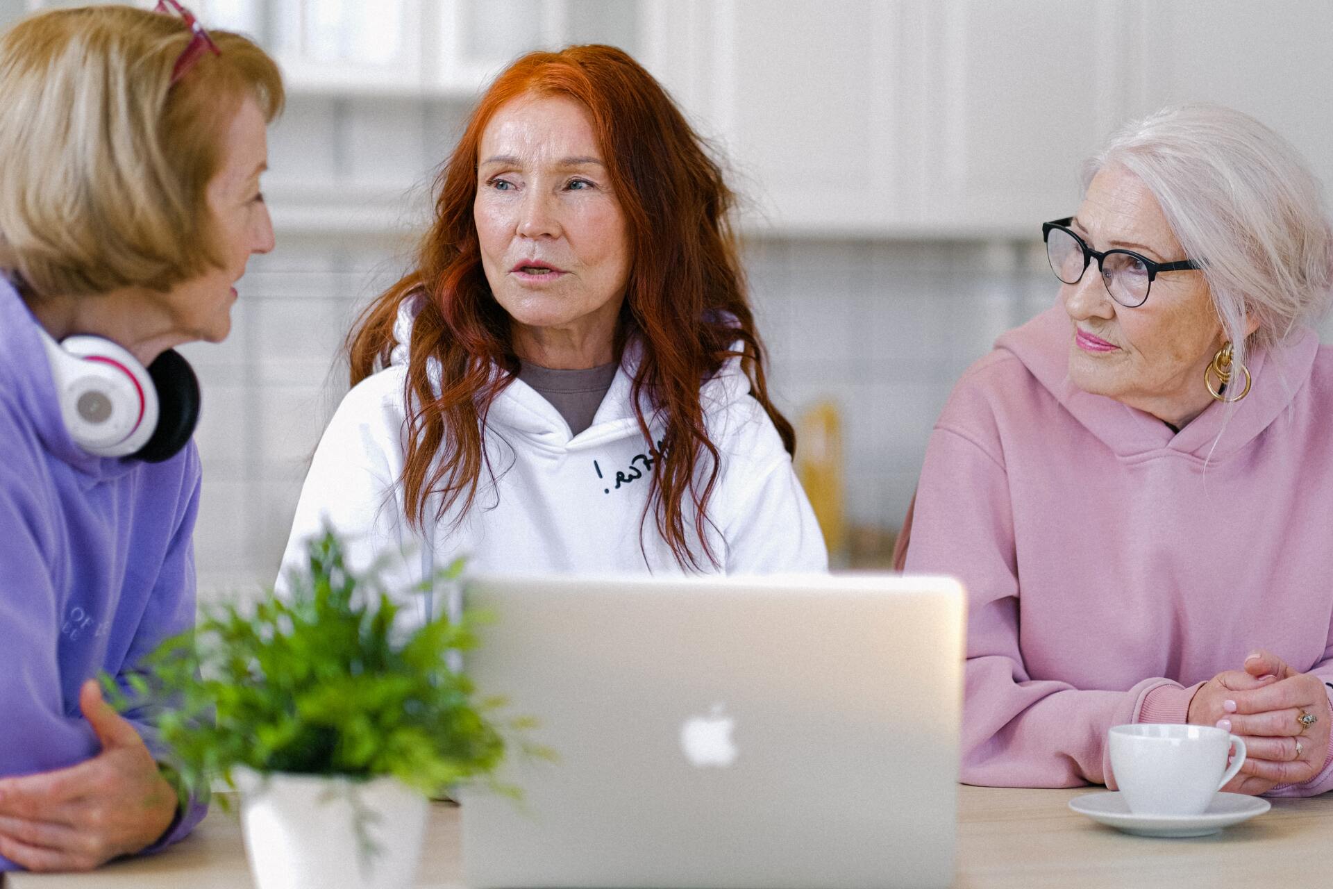Three women are sitting at a table looking at a laptop computer.