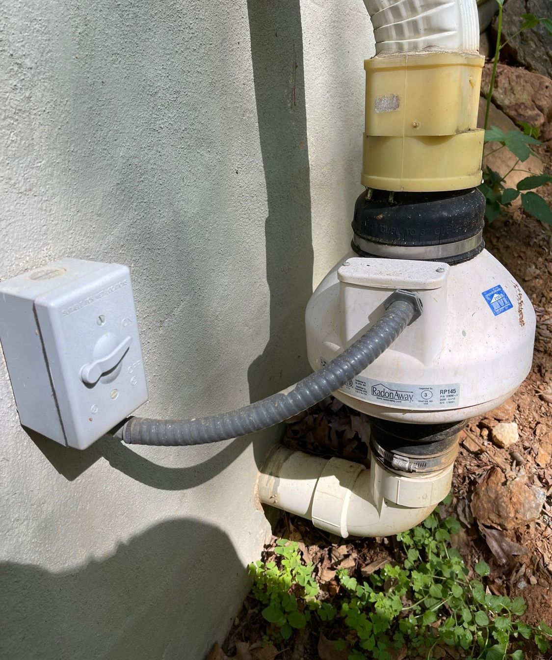 A white pipe with a hose attached to it is attached to a wall.