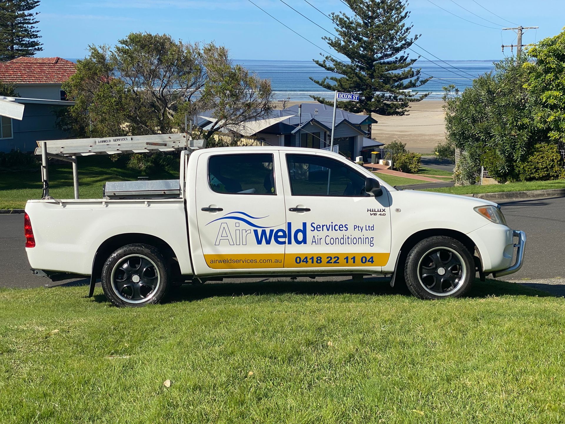 White pickup truck with business logo parked on grass, beach and houses in background. — Airweld Services Pty Ltd in Shellharbour, NSW