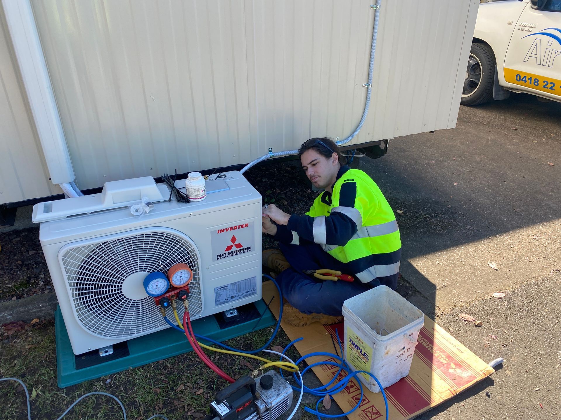 Person in safety vest fixing an outdoor air conditioning unit next to a white building. — Airweld Services Pty Ltd in Kiama, NSW