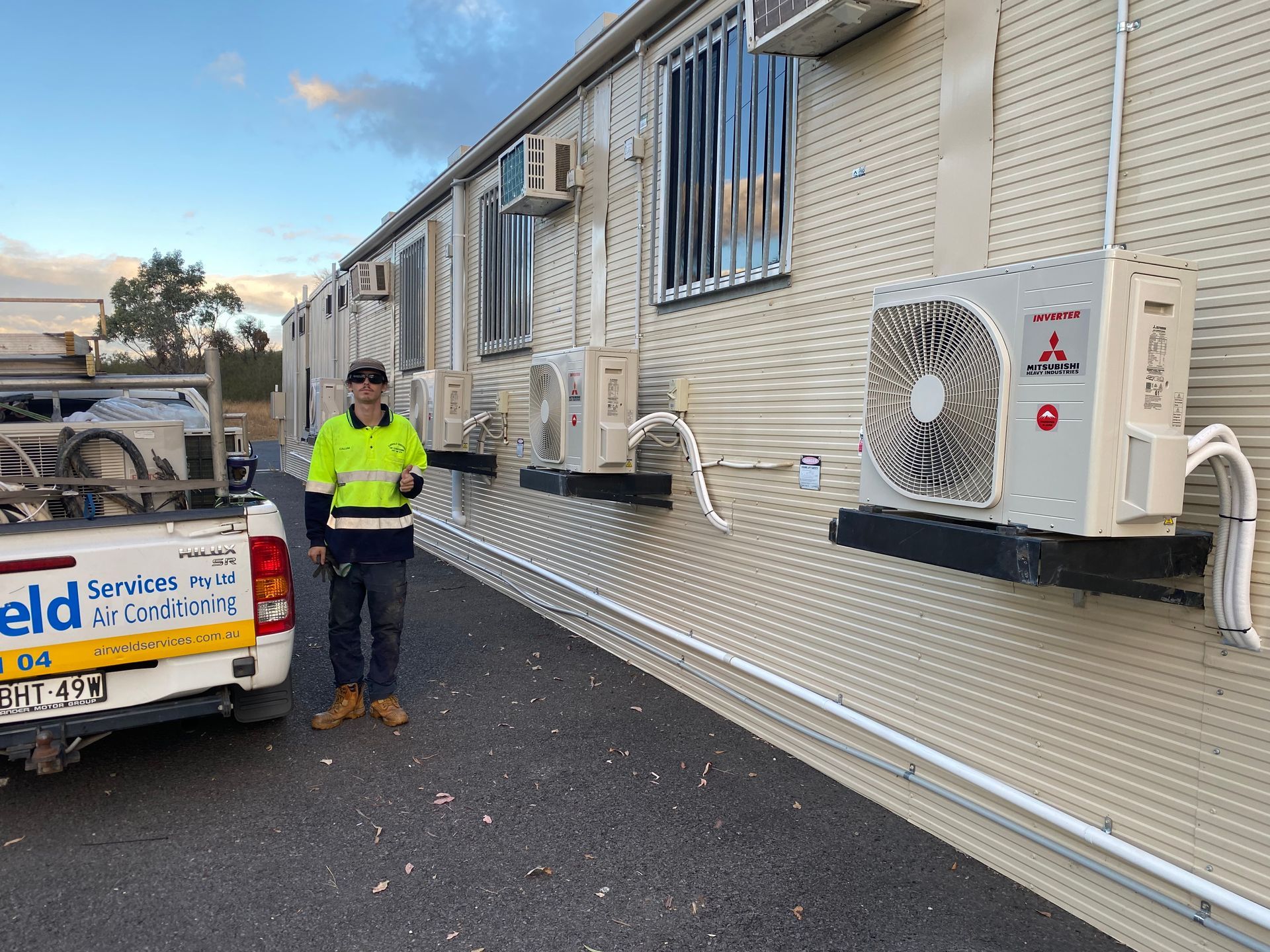 Man standing near a white building with several air conditioning units attached to the wall. A service truck is parked beside the building. — Airweld Services Pty Ltd in Shellharbour, NSW