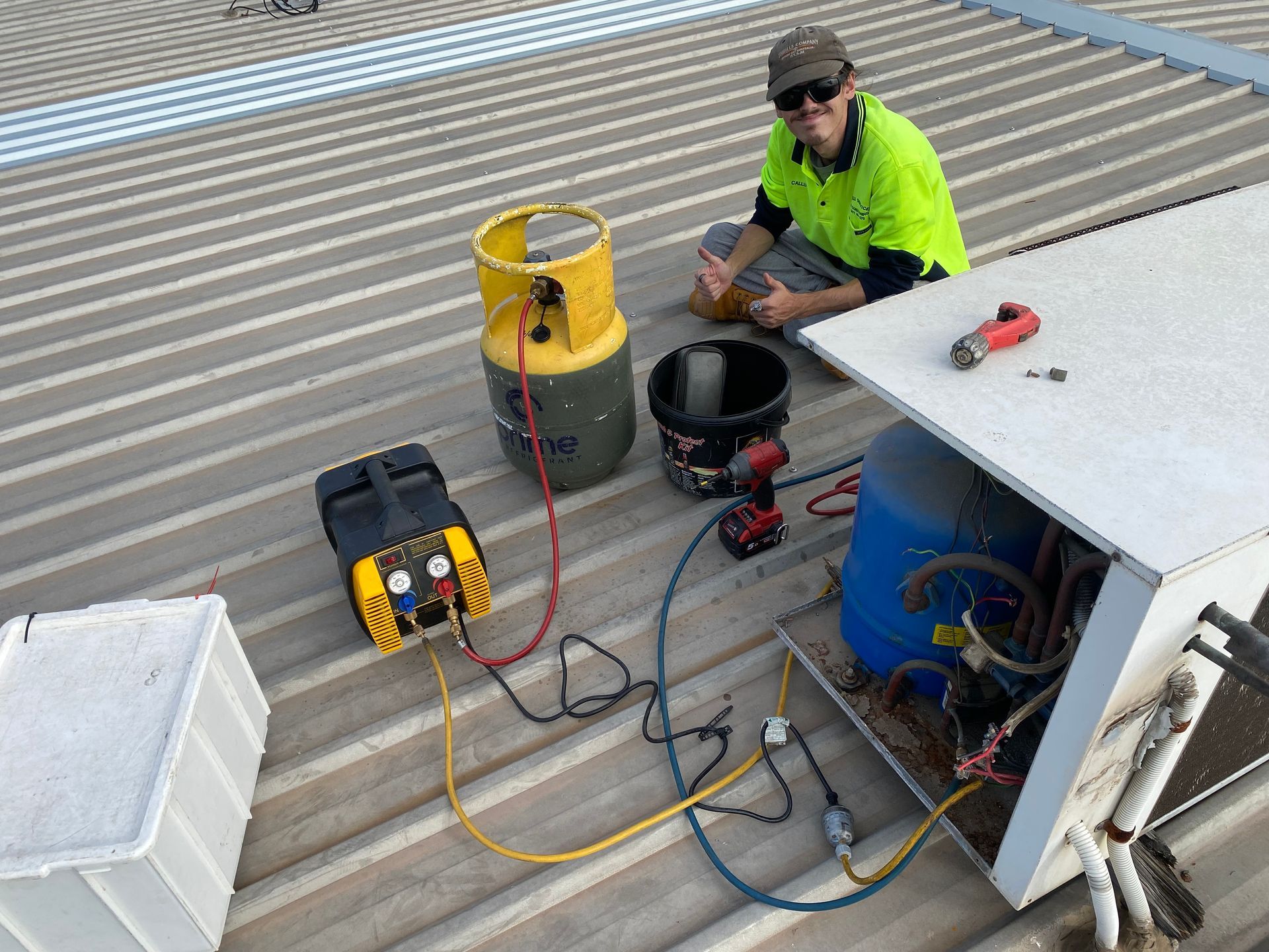 HVAC technician on a rooftop working on equipment with gauges, a refrigerant tank, and tools. — Airweld Services Pty Ltd in Shellharbour, NSW