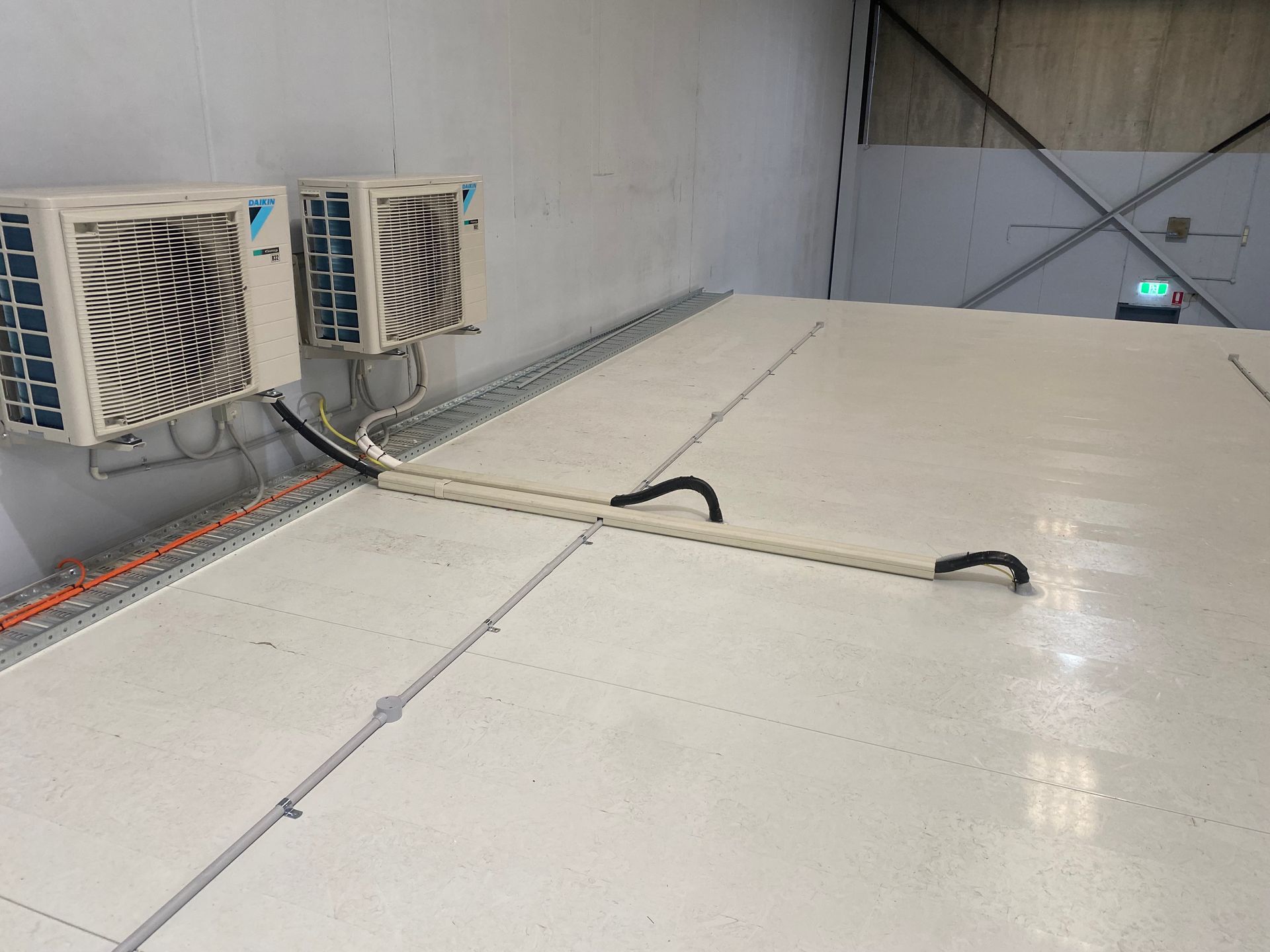 Two air conditioning units mounted on a wall; conduit runs across a white floor. — Airweld Services Pty Ltd in Ulladulla, NSW