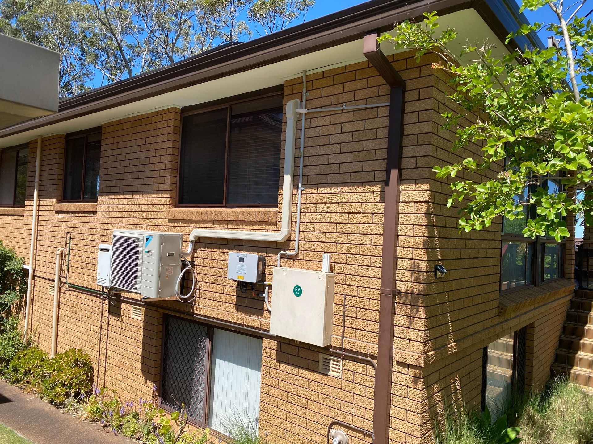 Brick building exterior with brown gutters, air conditioning units, and a window with a screen. — Airweld Services Pty Ltd in Shellharbour, NSW
