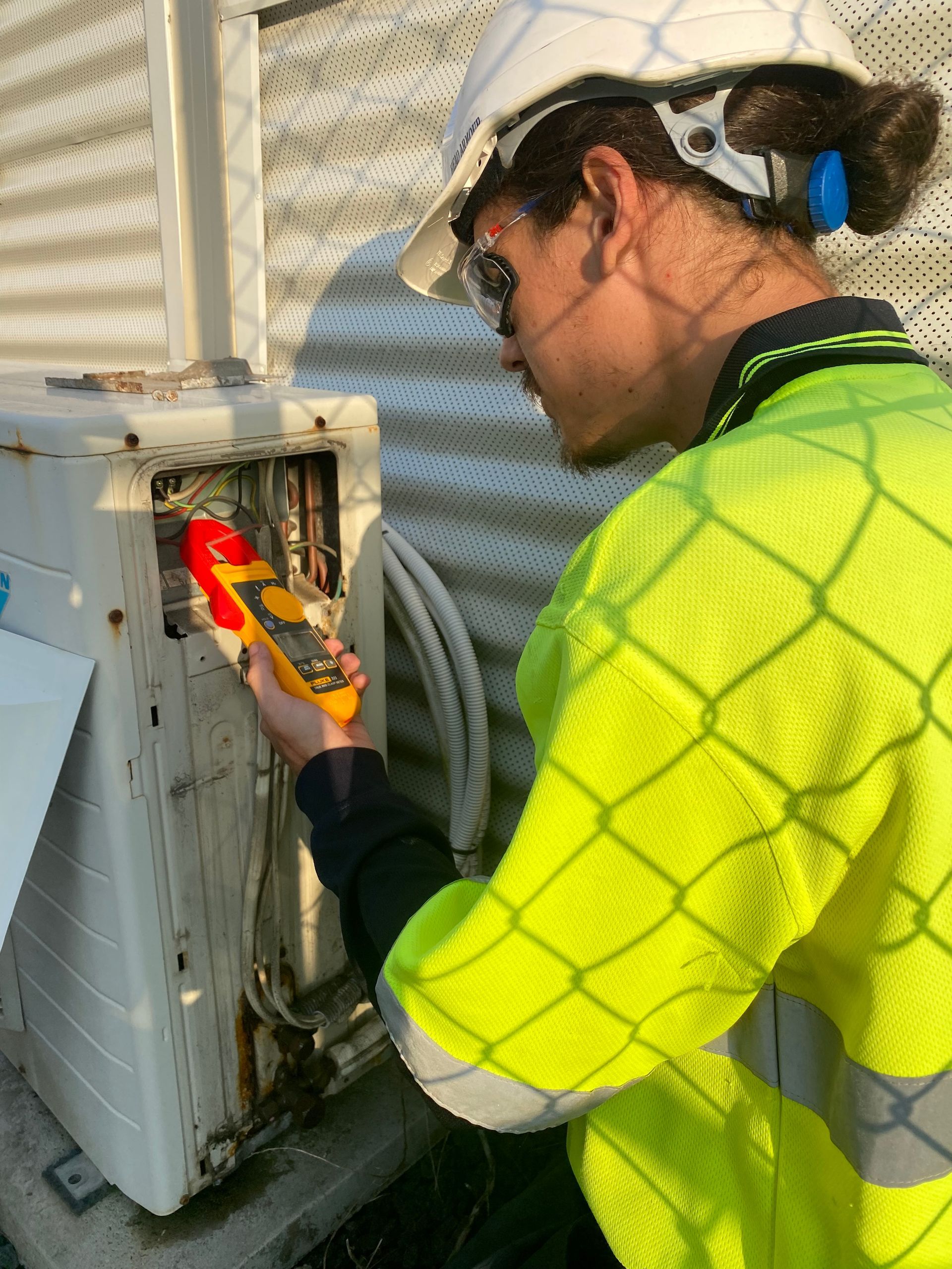 Person in safety gear inspecting outdoor AC unit with a yellow device. — Airweld Services Pty Ltd in Nowra, NSW