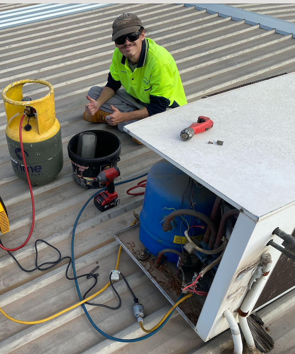HVAC technician on roof, repairing unit. Yellow refrigerant tank, tools, blue component, thumbs up  — Airweld Services Pty Ltd in Shellharbour, NSW