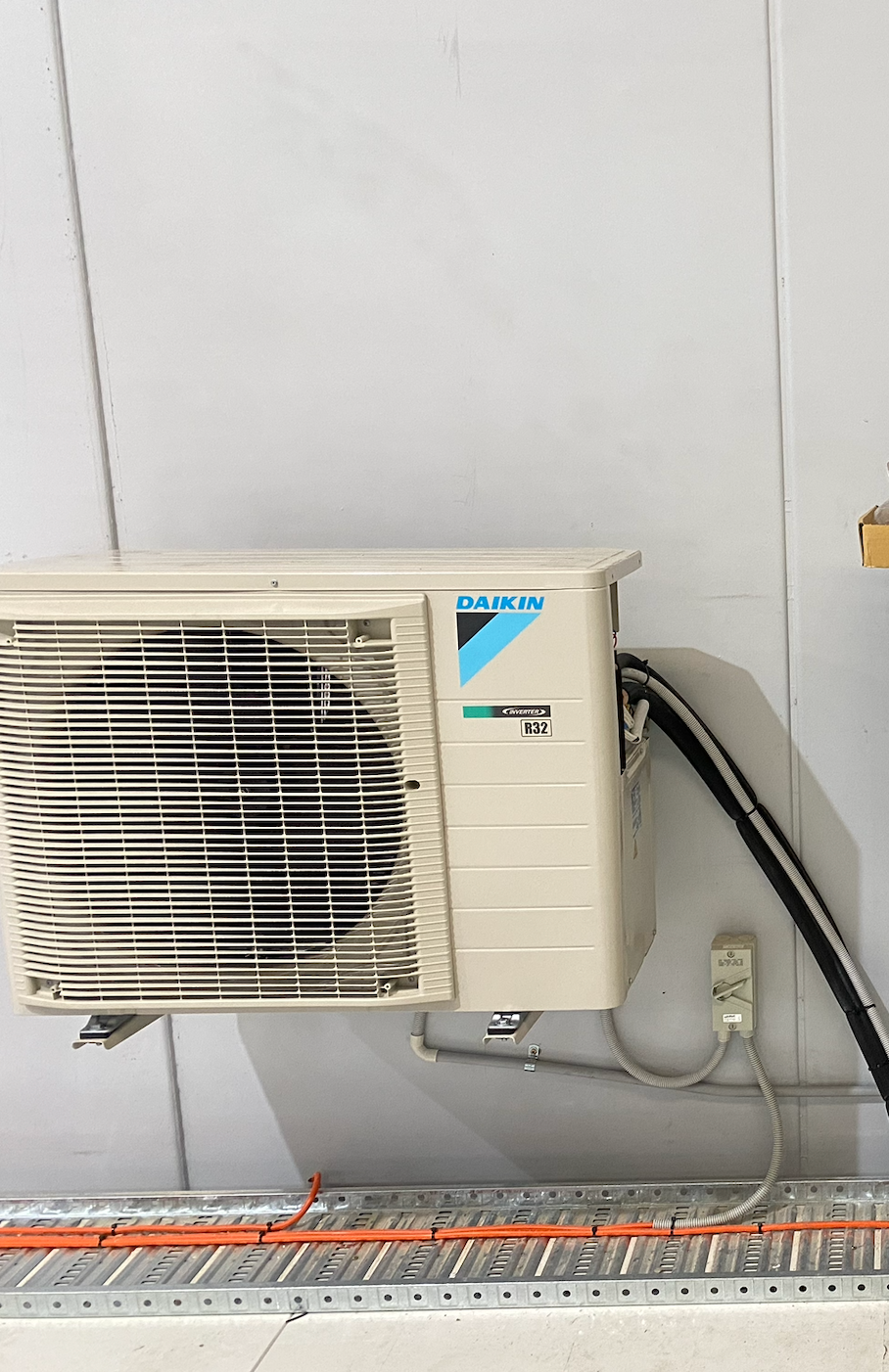 White Daikin air conditioner mounted on a white wall, with electrical conduits and cable trays below  — Airweld Services Pty Ltd in Shellharbour, NSW