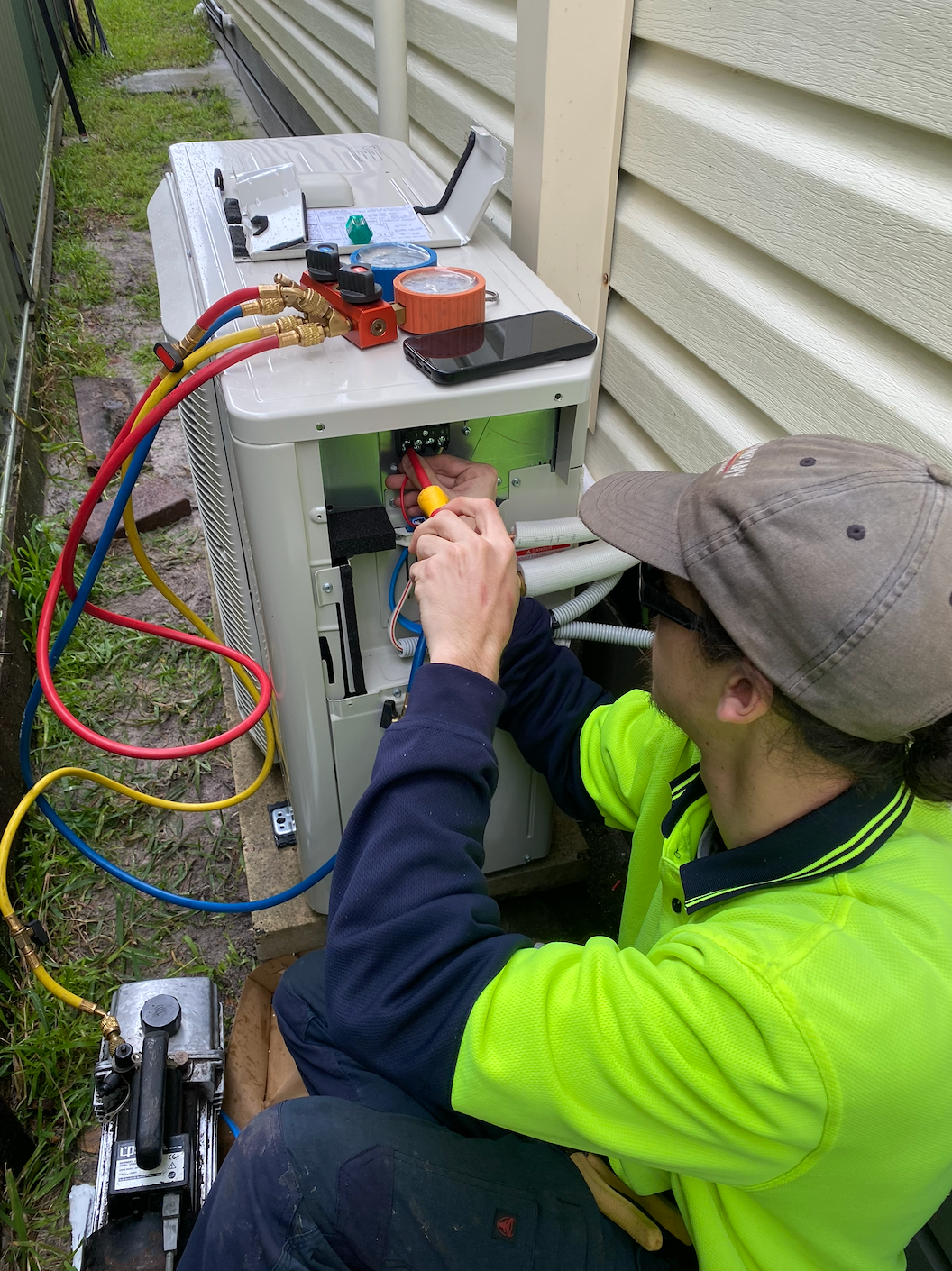 Person repairing an outdoor air conditioning unit, using tools and gauges — Airweld Services Pty Ltd in Shellharbour, NSW