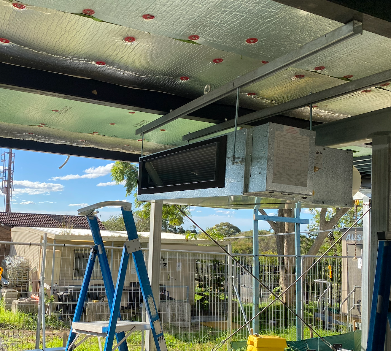Air conditioning unit installed on a ceiling, with silver insulation and metal frame. A blue ladder is in the foreground — Airweld Services Pty Ltd in Wollongong, NSW