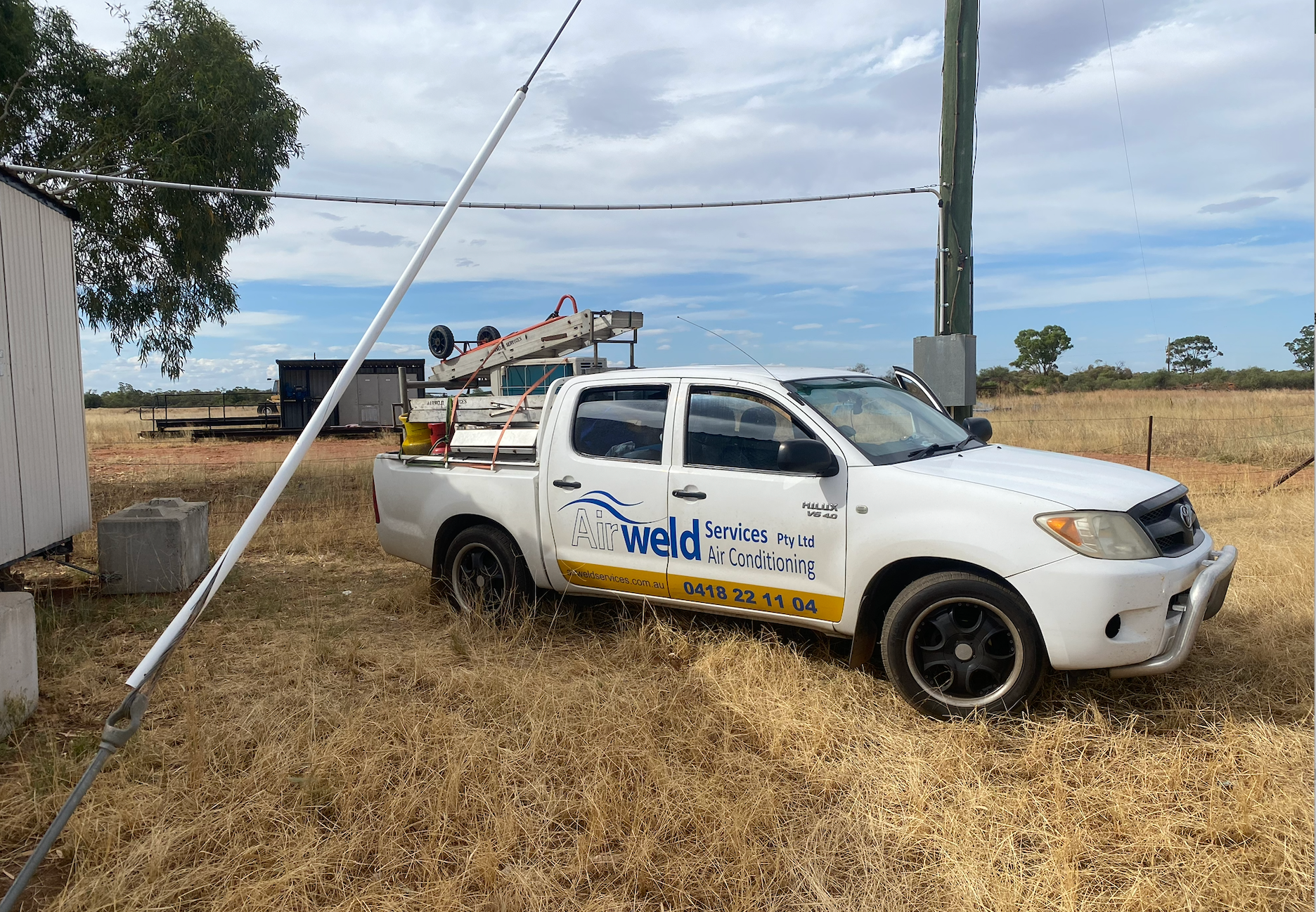White work truck in a field, with a utility pole and raised bucket, cloudy sky — Airweld Services Pty Ltd in Wollongong, NSW