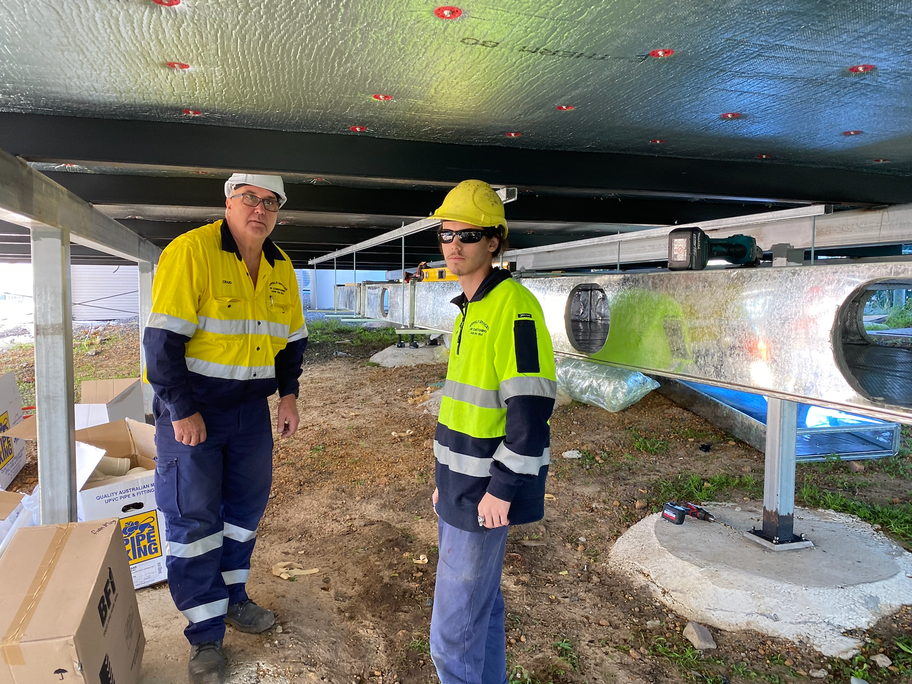 Two construction workers under a building, one wearing a yellow hard hat and vest, the other in a yellow vest  — Airweld Services Pty Ltd in Wollongong, NSW