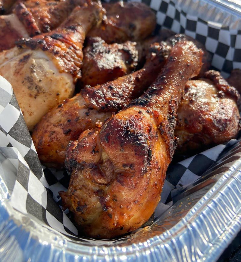 A tin foil container filled with chicken legs and thighs on checkered paper.