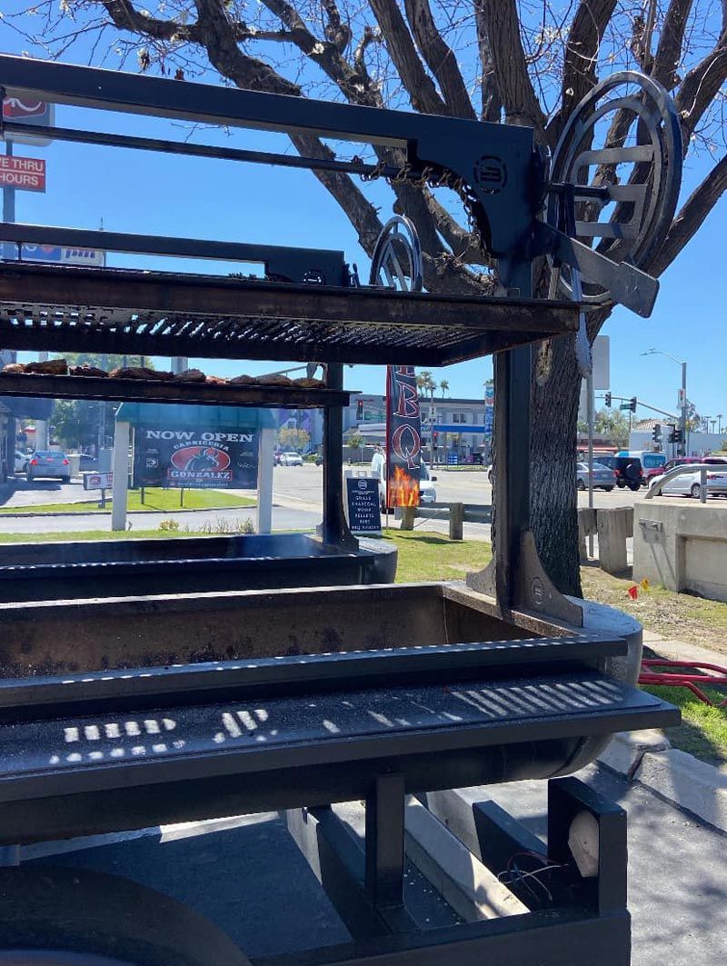 A large grill is sitting under a tree in a parking lot.