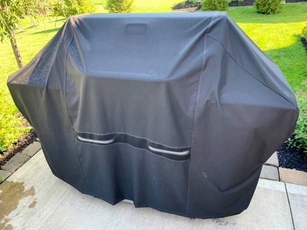 A grill with a black cover on it is sitting on a patio.