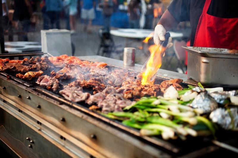 A person is cooking meat and vegetables on a grill.