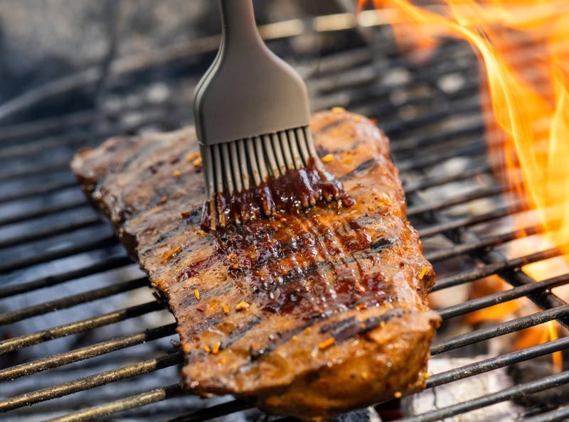 A steak is being brushed with barbecue sauce on a grill.