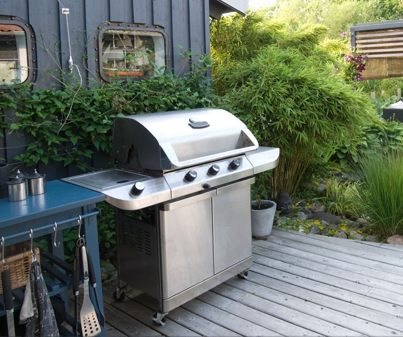 A grill is sitting on a wooden deck in front of a house.