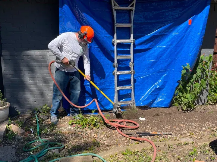 A man is standing in front of a blue tarp holding a hose.