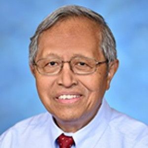 A man wearing glasses and a tie is smiling for the camera.