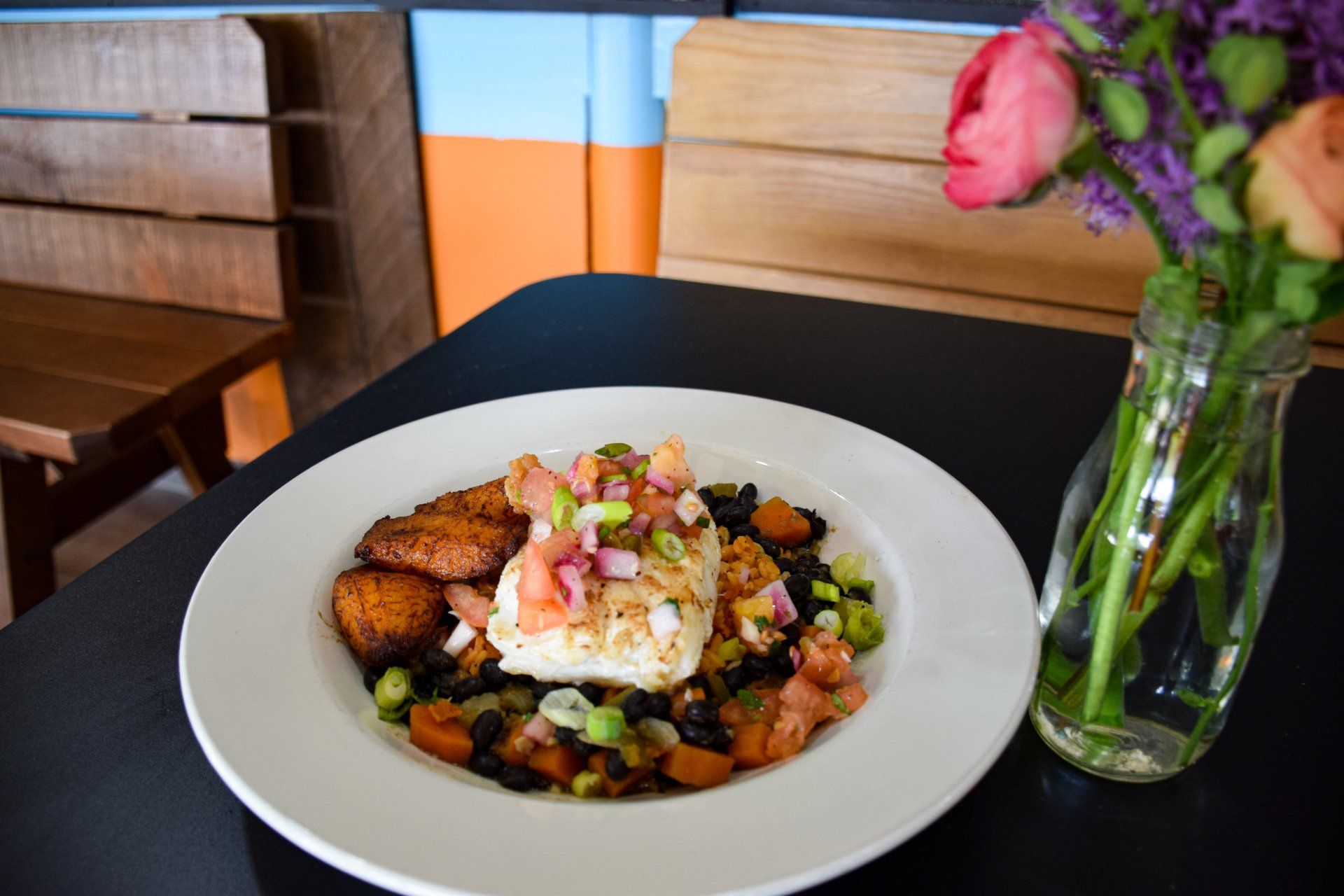 A plate of food is sitting on a table next to a vase of flowers.