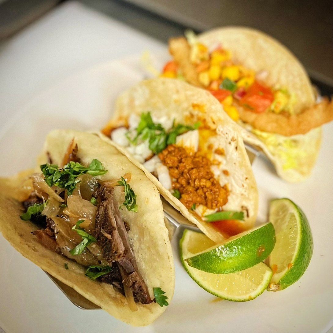 A white plate topped with three tacos and lime wedges.