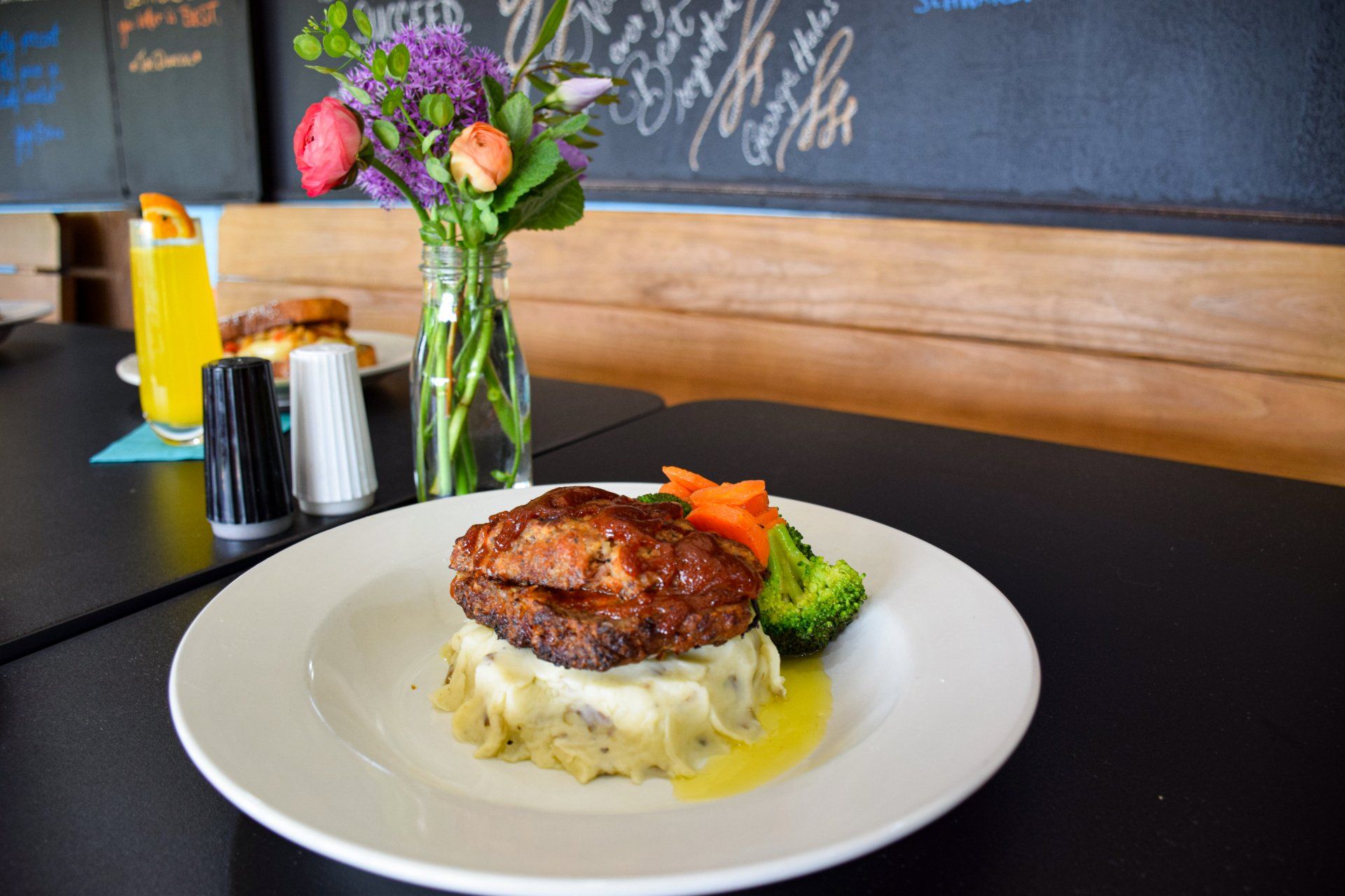 A plate of food on a table with a vase of flowers in the background.