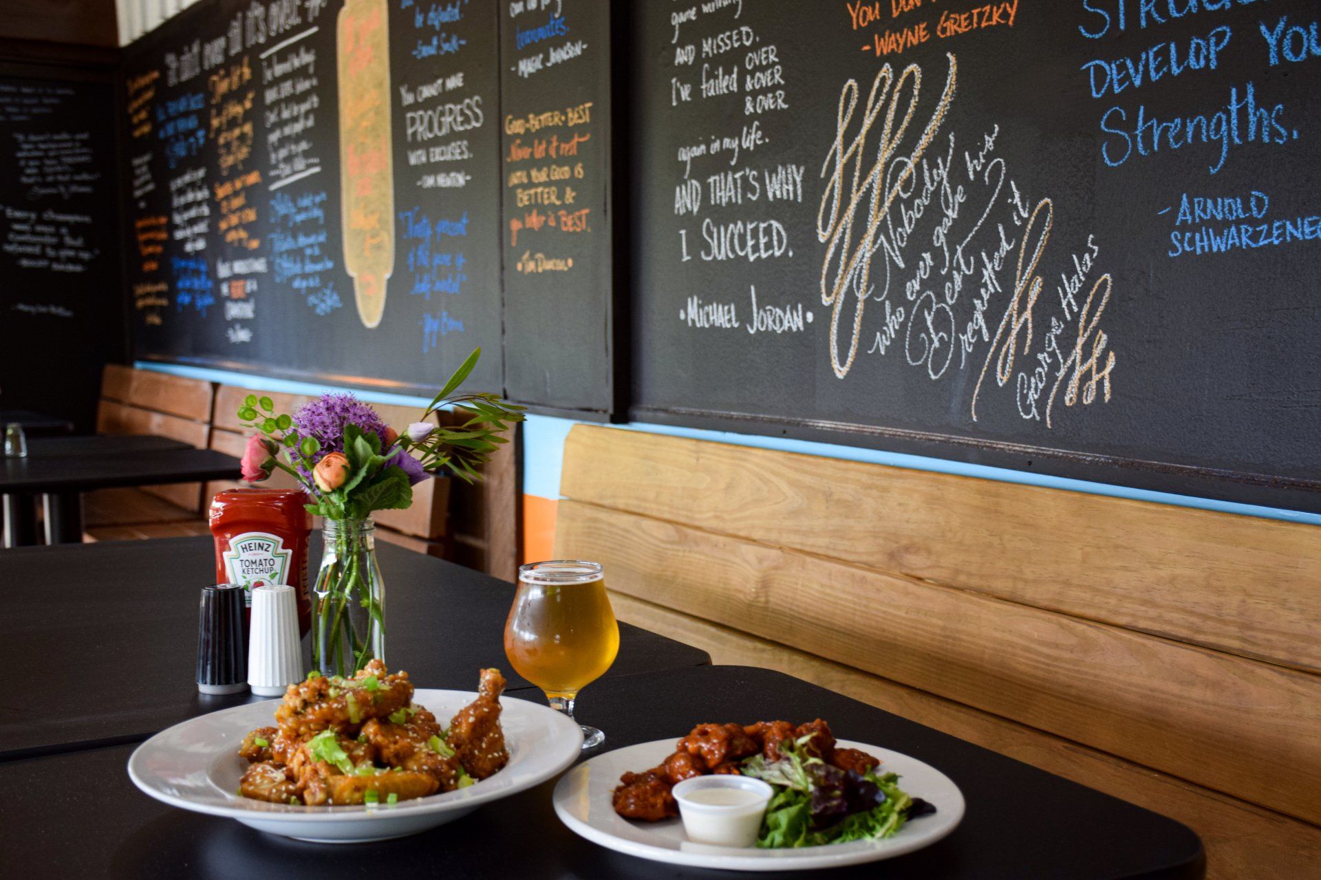 Two plates of food and a glass of beer on a table in front of a chalkboard.