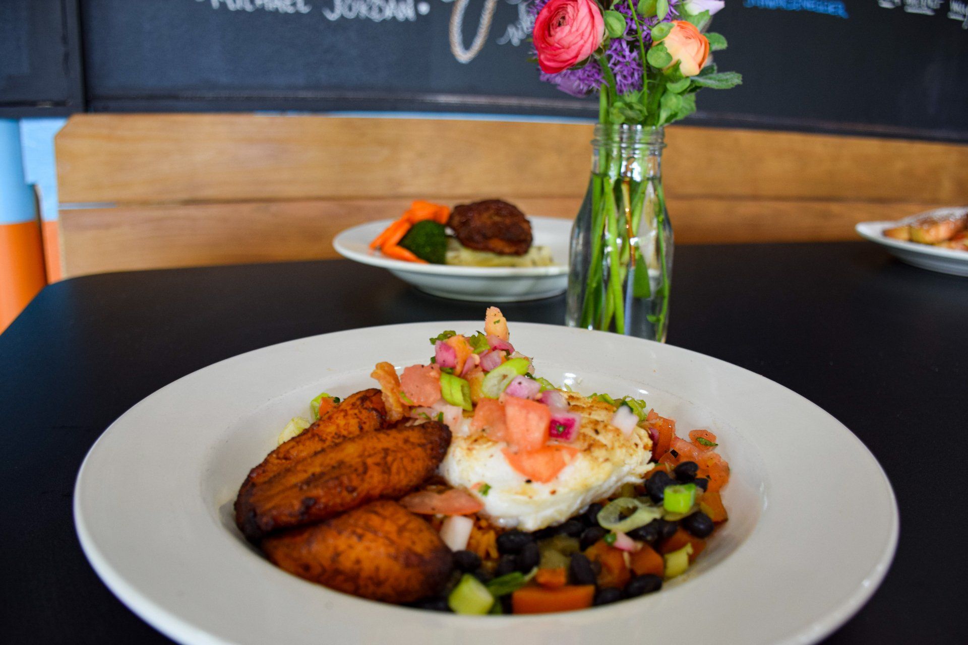A plate of food is sitting on a table next to a vase of flowers.