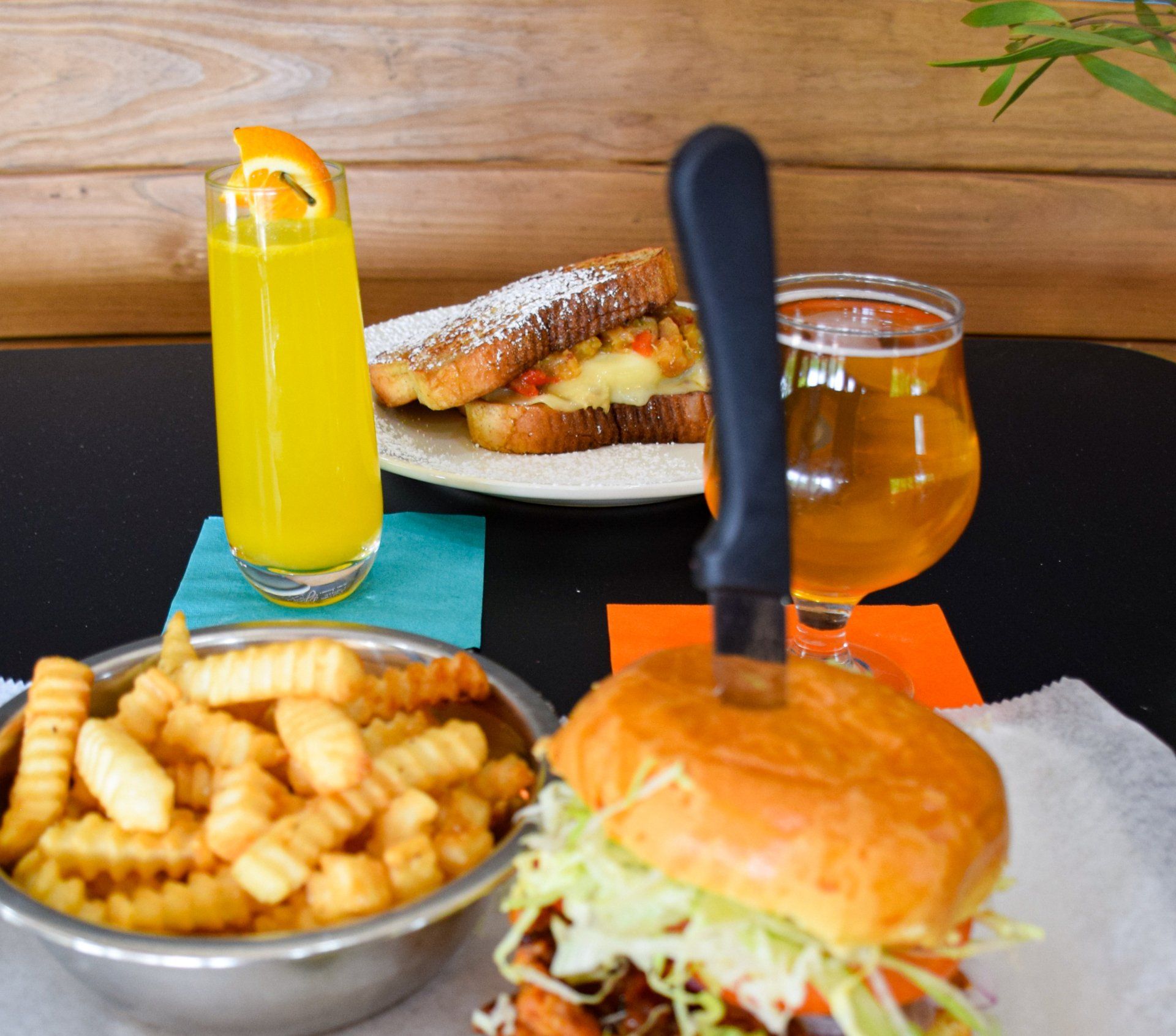A bowl of french fries sits next to a sandwich and a glass of orange juice