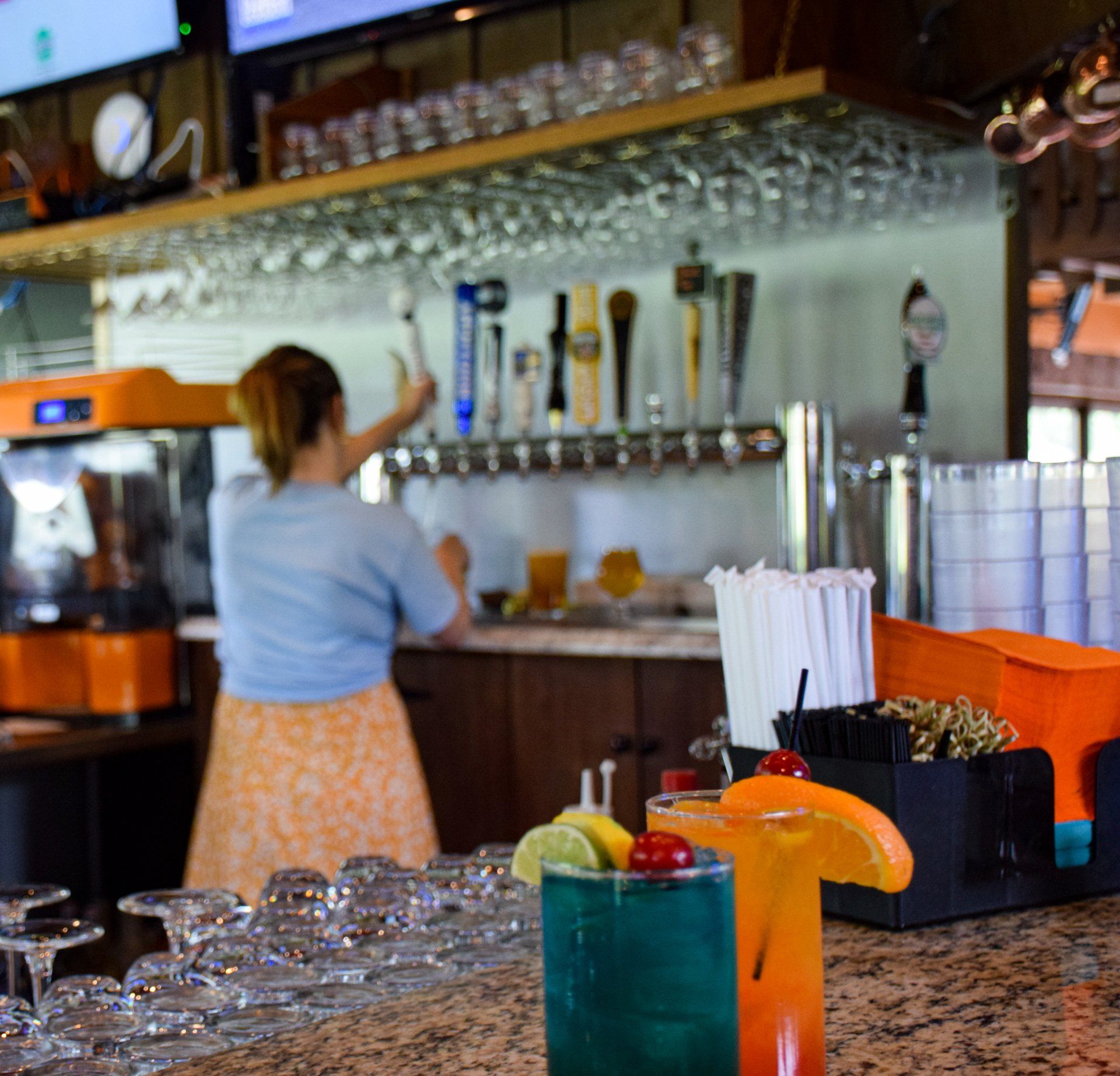 A woman is standing behind a bar preparing drinks.