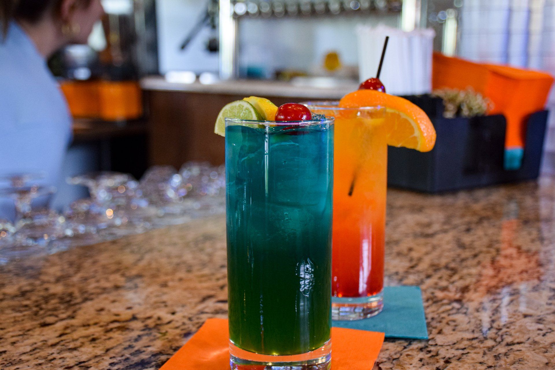 Two colorful drinks are sitting on a bar counter.