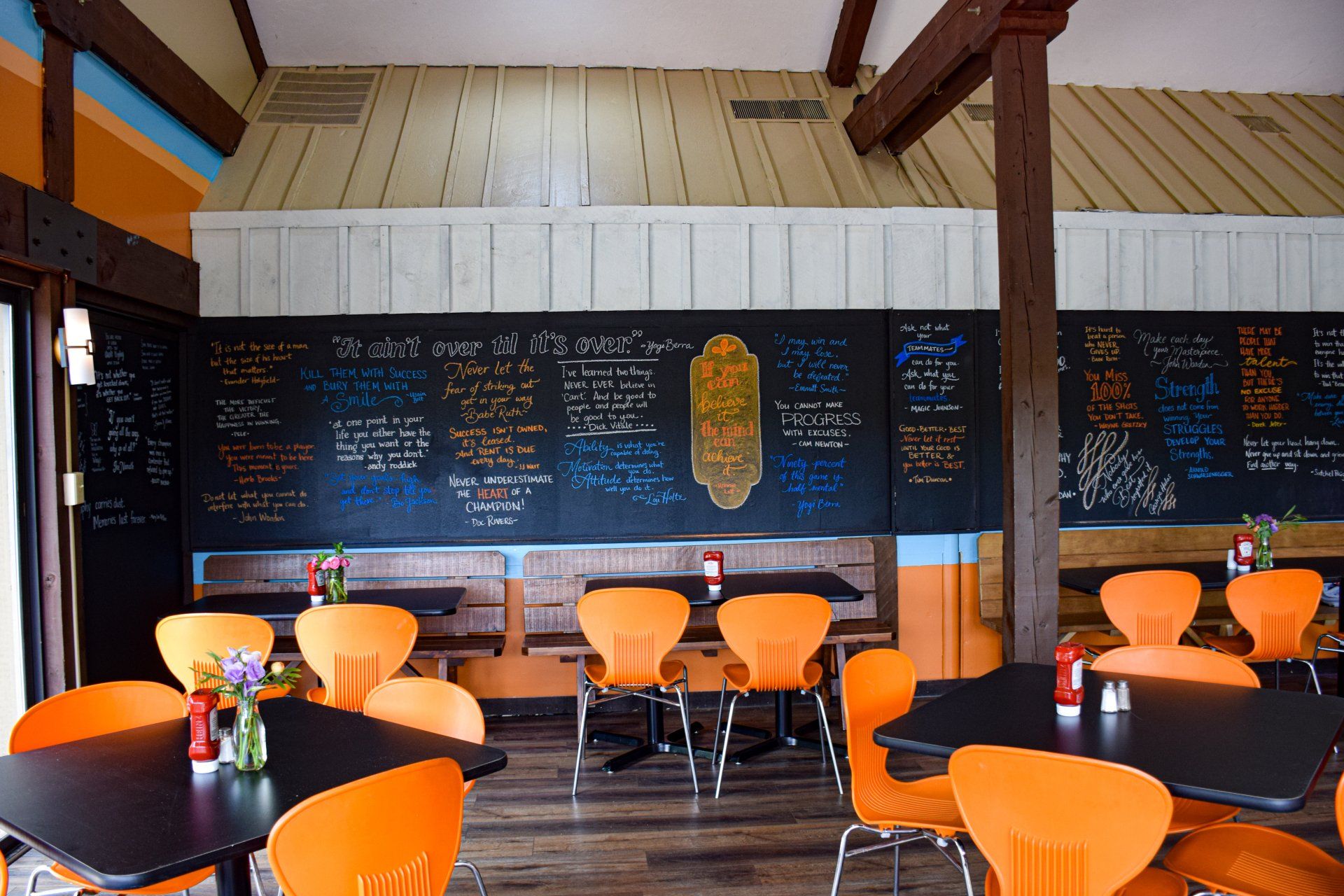 A restaurant with tables and chairs and a chalkboard on the wall