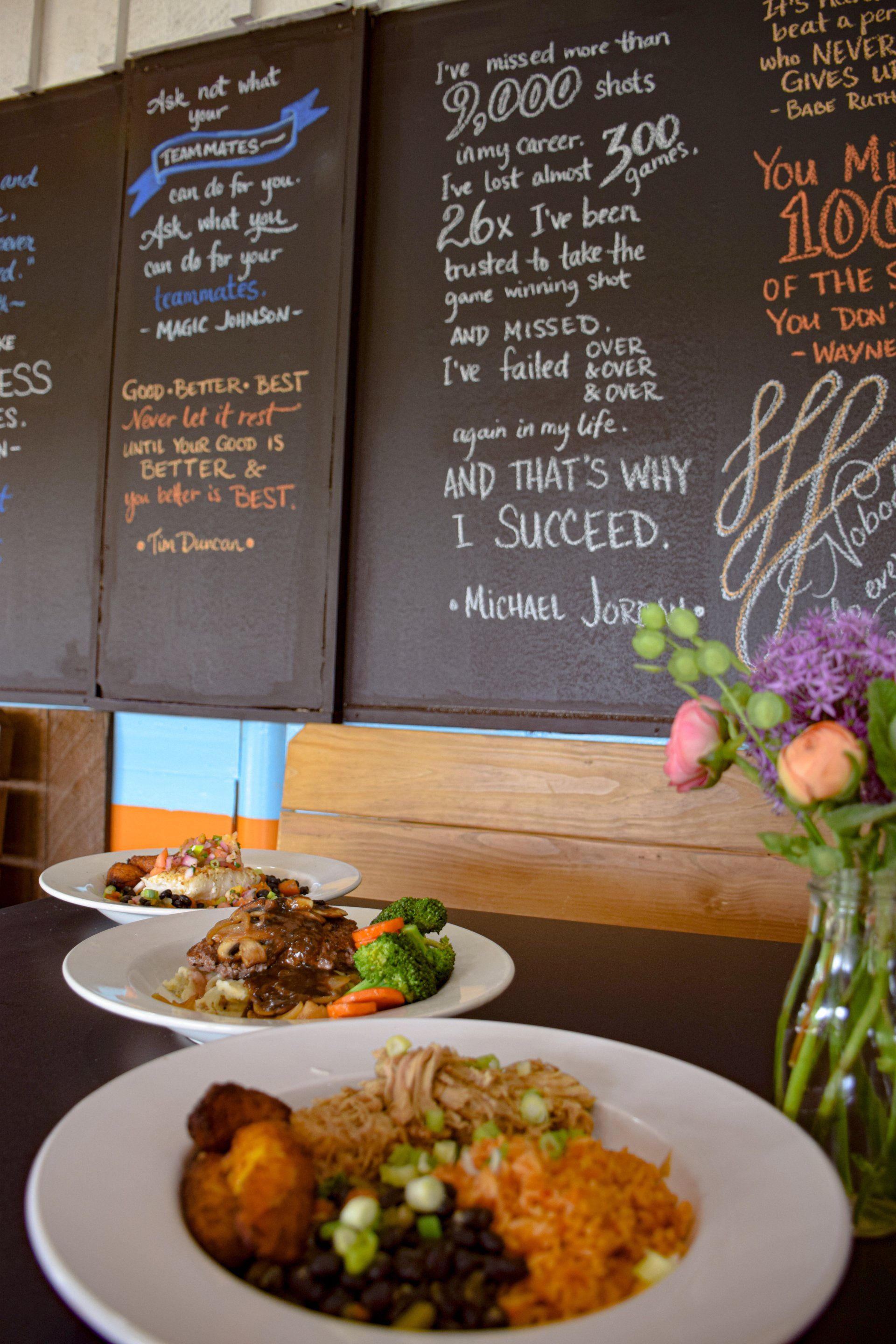 Three plates of food are on a table in front of a chalkboard that says