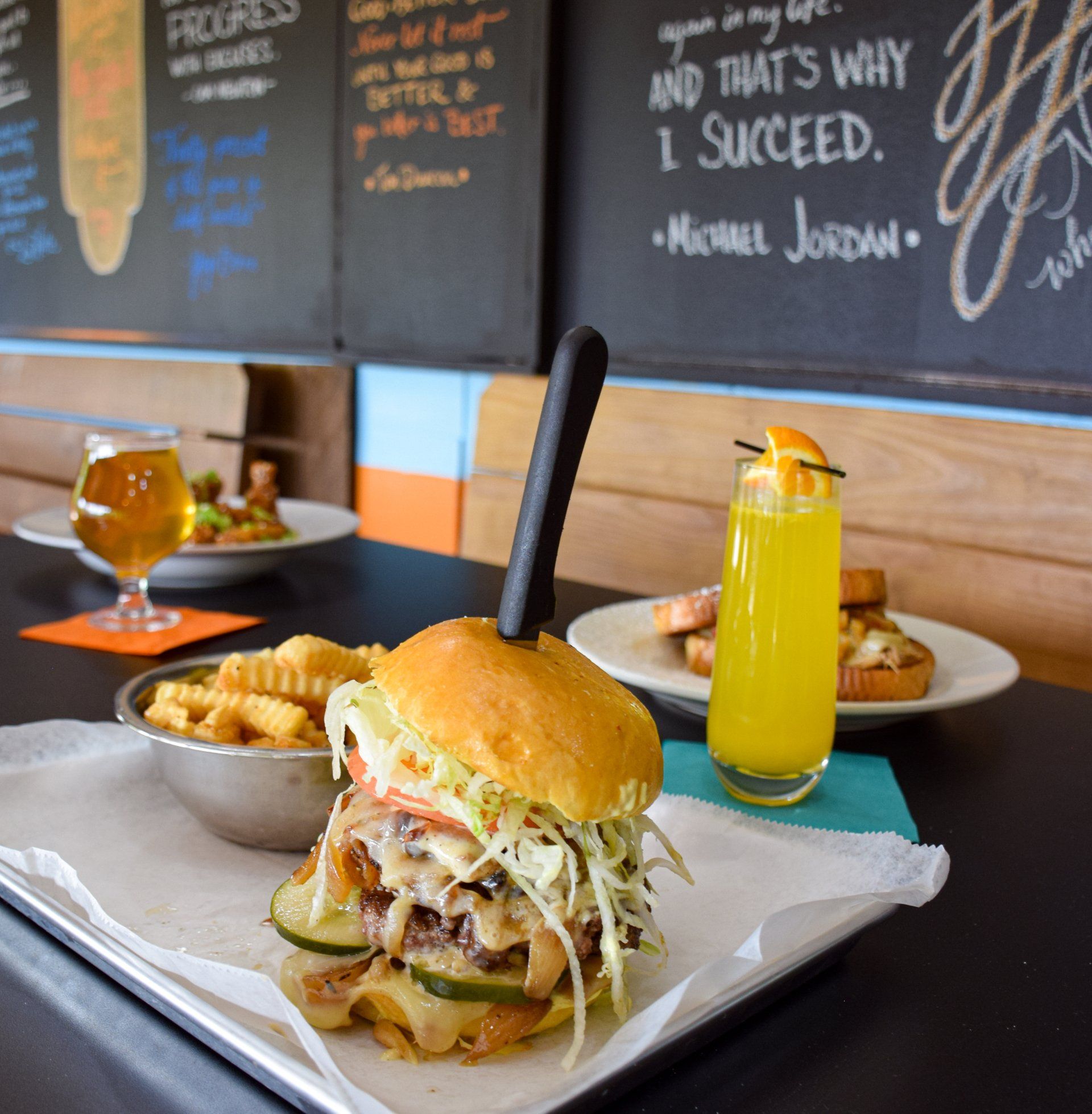 A hamburger is on a plate next to a glass of orange juice