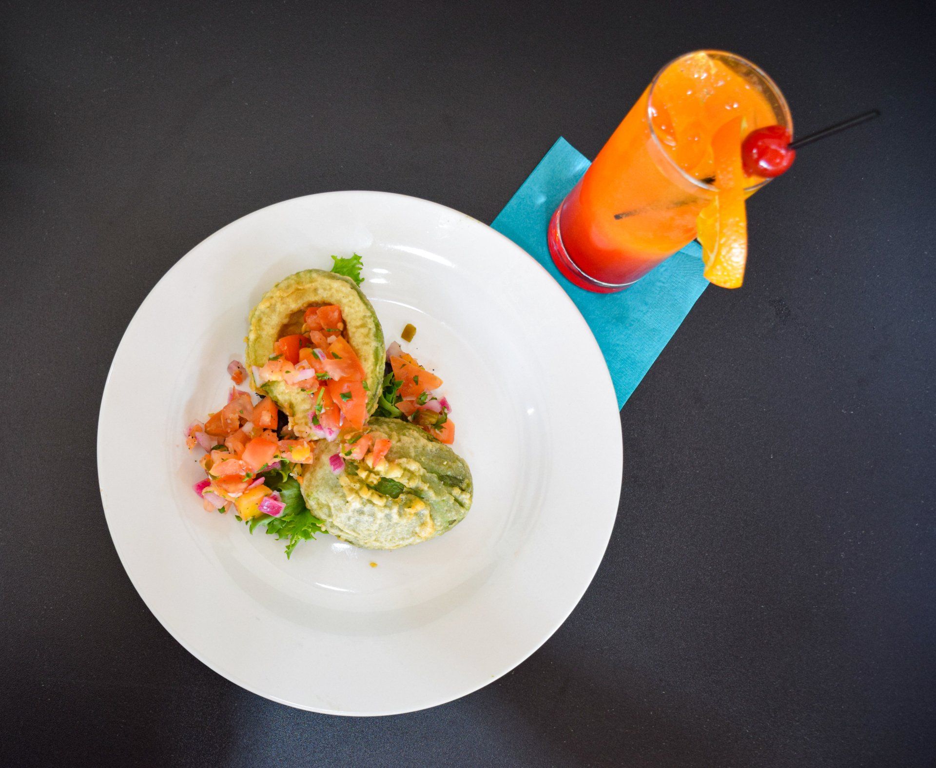 A plate of food next to a drink with a cherry on top