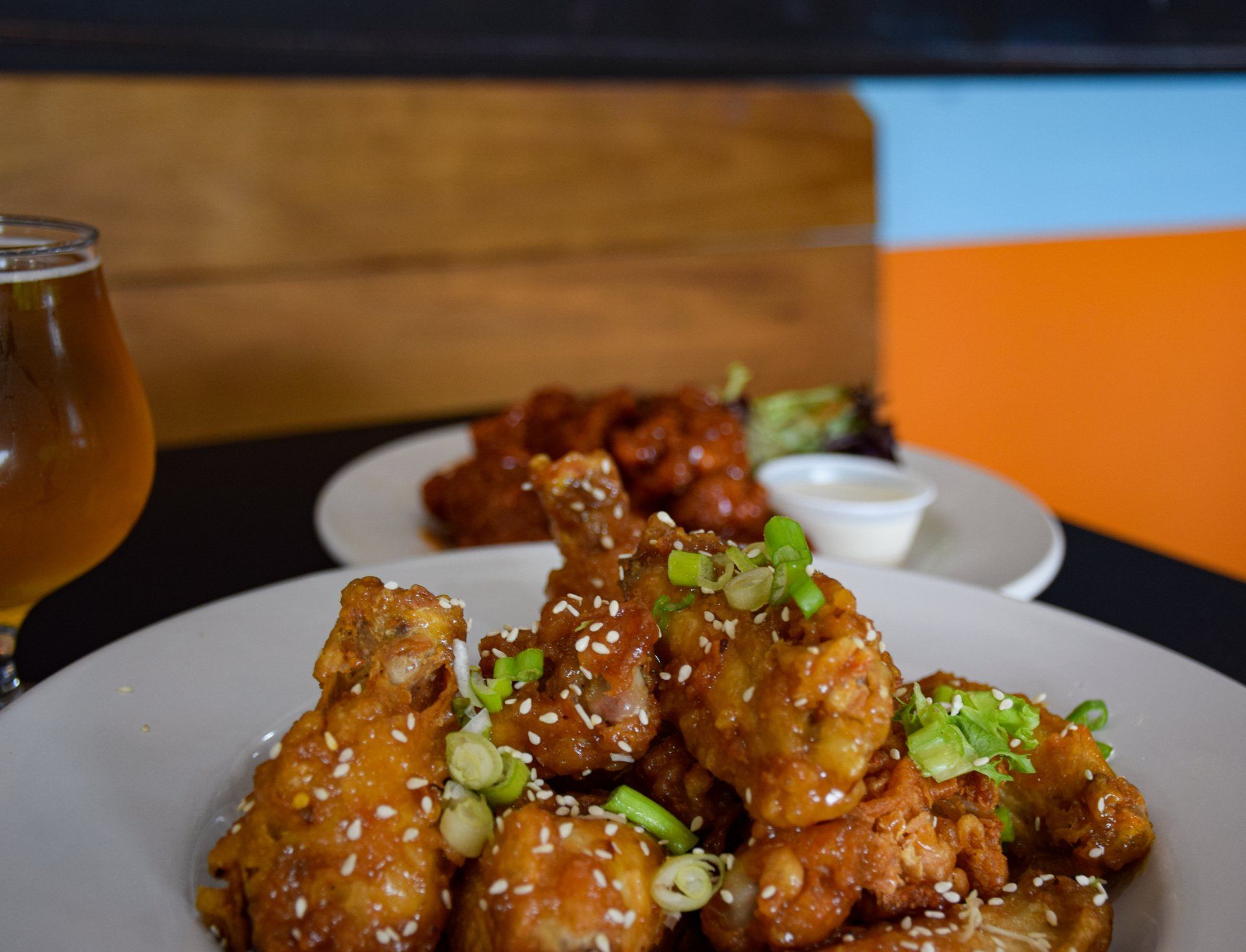 A plate of chicken wings with sesame seeds and green onions on a table next to a glass of beer.