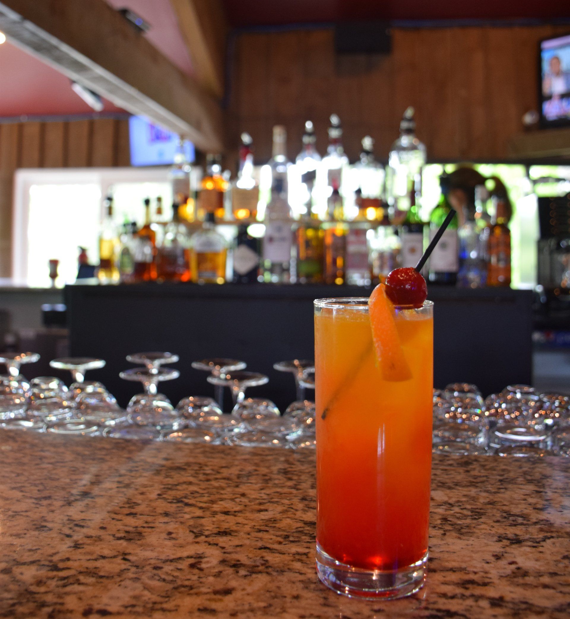 A tall glass of orange liquid with a cherry on top