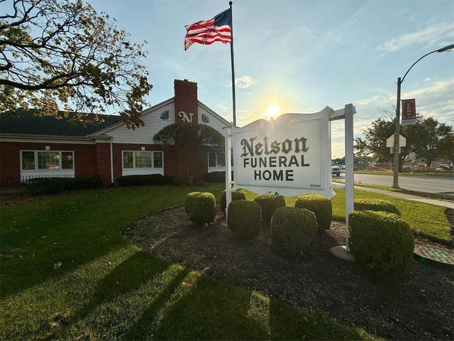 Nelson Funeral Home sign with an American flag; red brick building, sunny day.