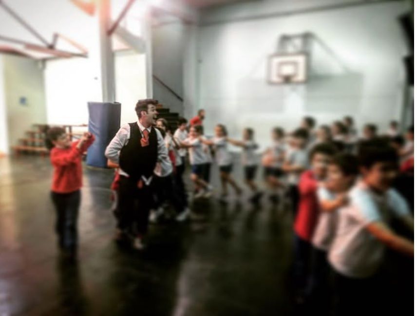 Clown leads a group of children in a gymnasium, all participating in an activity.