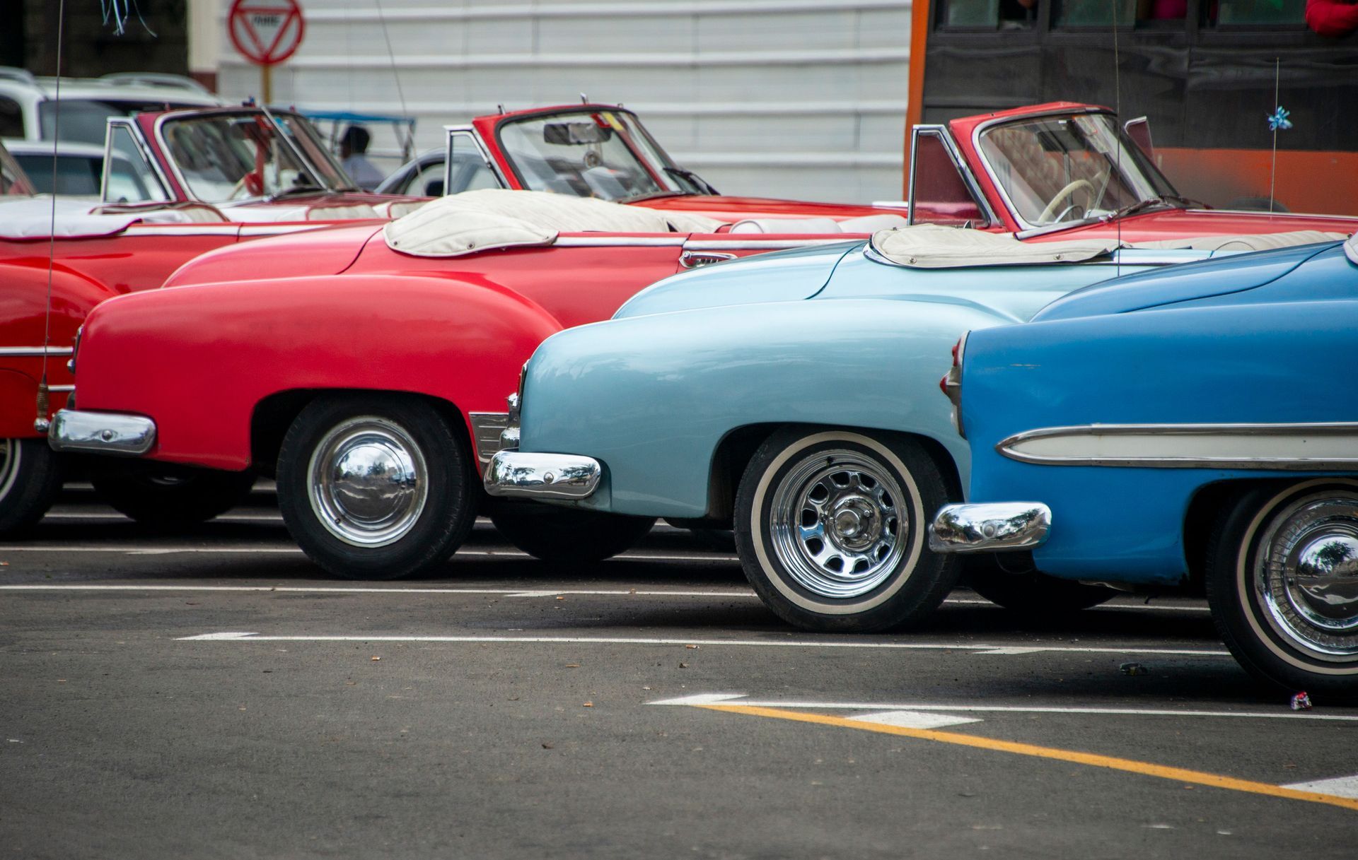 A row of old cars are parked in a parking lot.