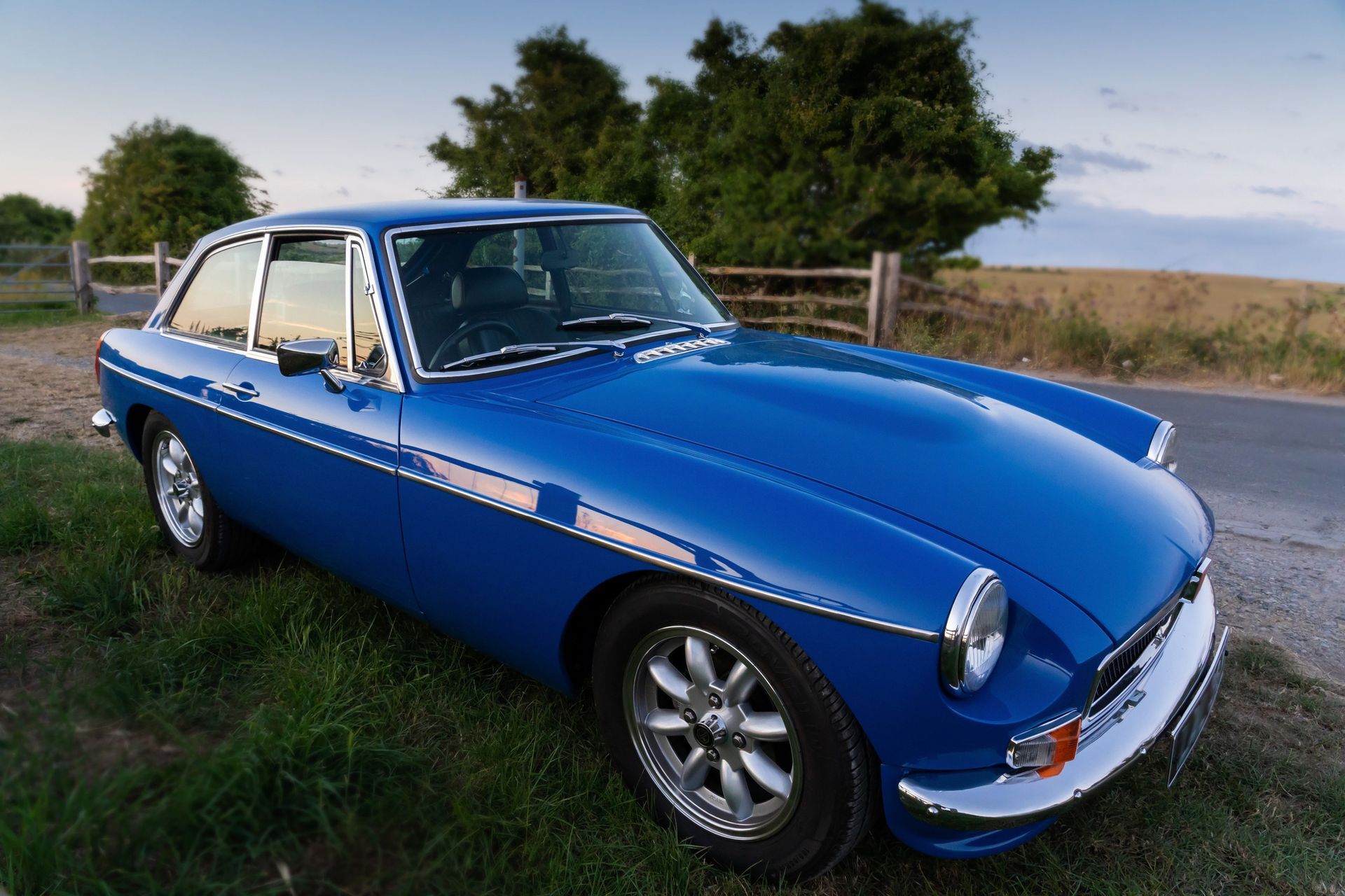 A bright blue british classic car, is parked up at the side of a country lane.