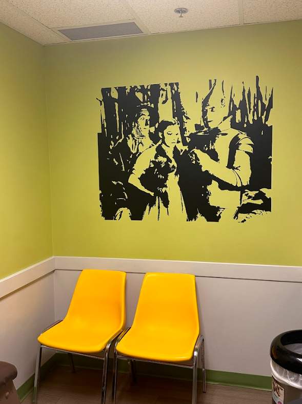A waiting room with two yellow chairs and a picture on the wall