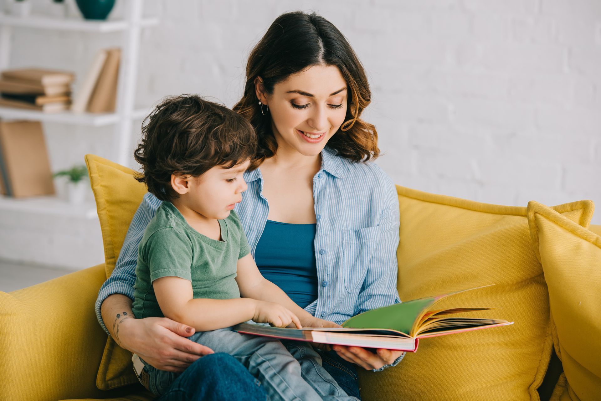 Woman and child on yellow couch, reading a book together.